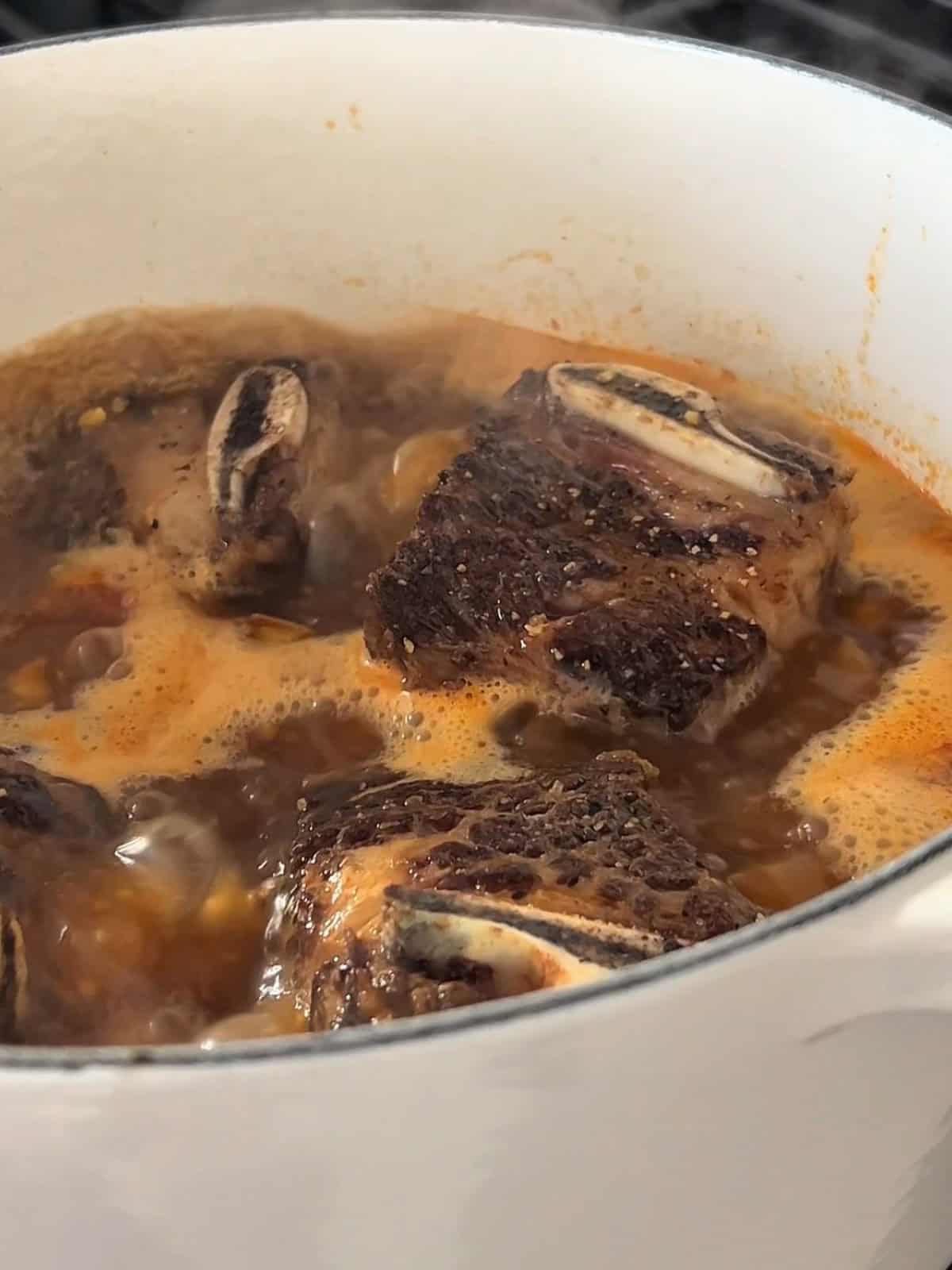 Bone in short ribs simmering in broth mixture in a dutch oven.