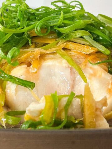 Side shot of the flaky steamed fish garnished with ginger and scallions.
