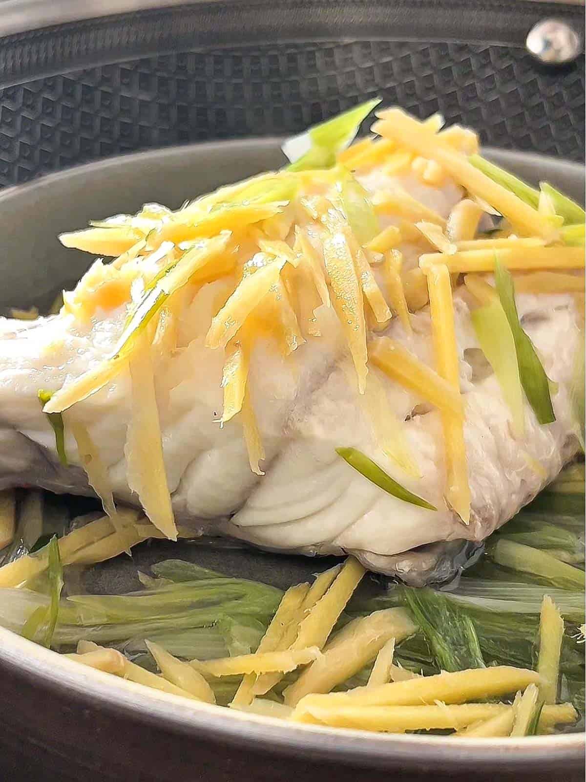 Cooked steamed fish with ginger and garlic on top.