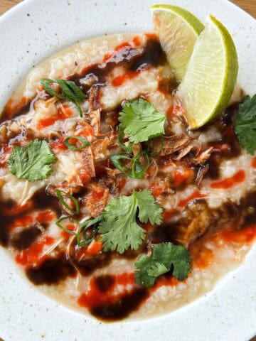 Overhead shot of pho congee drizzled with hoisin sauce and sriracha and topped with herbs in a 1x1 format.