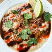 Shot of pho congee drizzled with hoisin sauce and sriracha and topped with herbs in a 1x1 format.