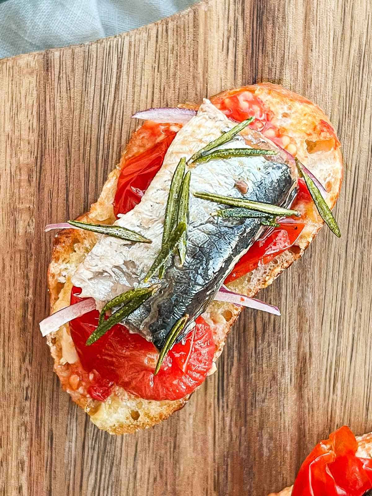 Close up of sardine on roasted tomato on a baguette slice.