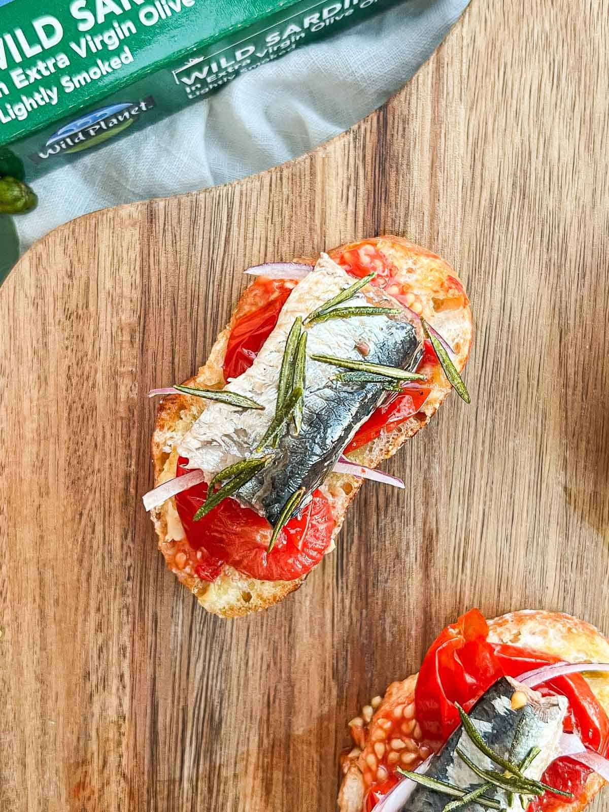 Sardine on roasted tomato on a baguette slice.