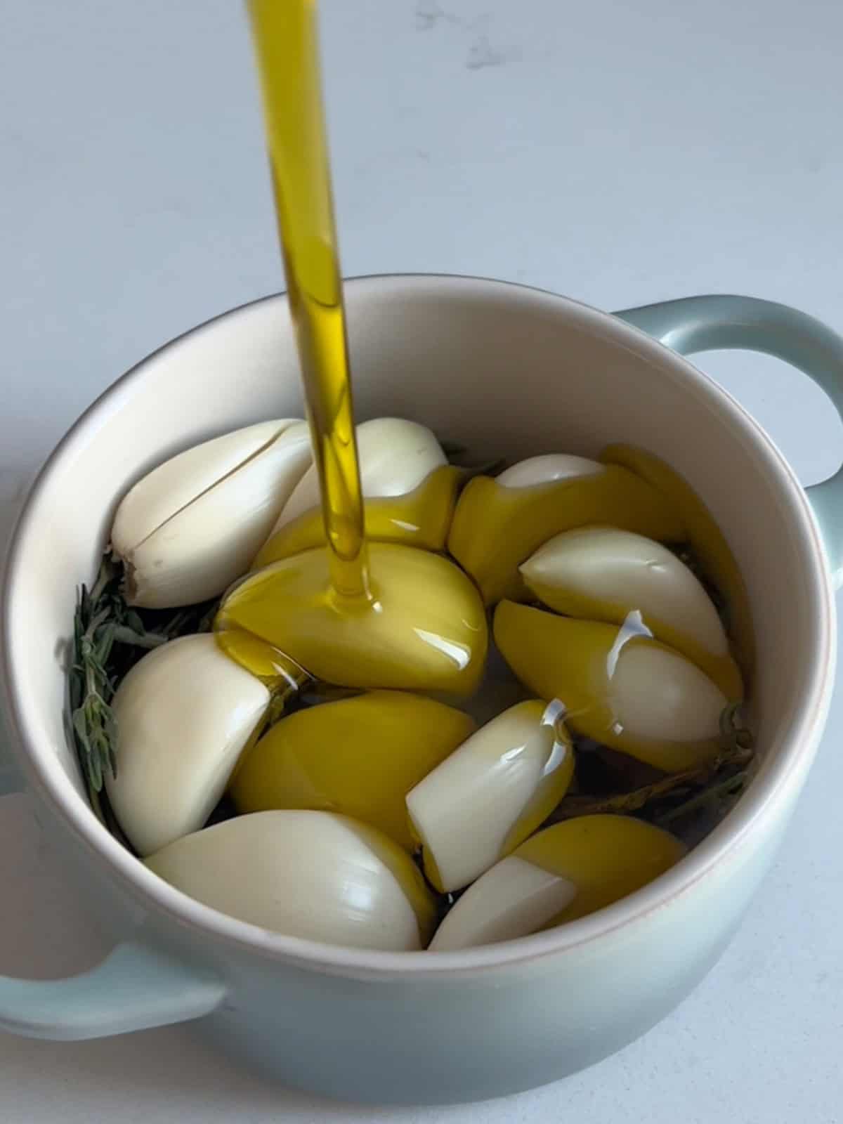 Garlic, herbs, and olive oil in mini cocotte dish.