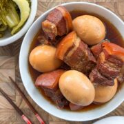 Braised pork belly and hard boiled eggs in a bowl with chopsticks on the side and pickled mustard greens.