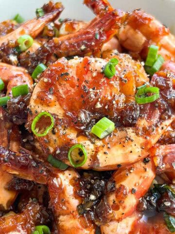 Close up shot of caramelized shrimp in a bowl garnished with scallions and black pepper.