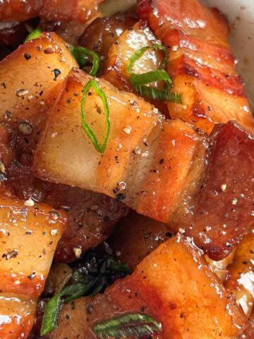 A side 1x1 shot of caramelized pork belly garnished with black pepper and scallions.