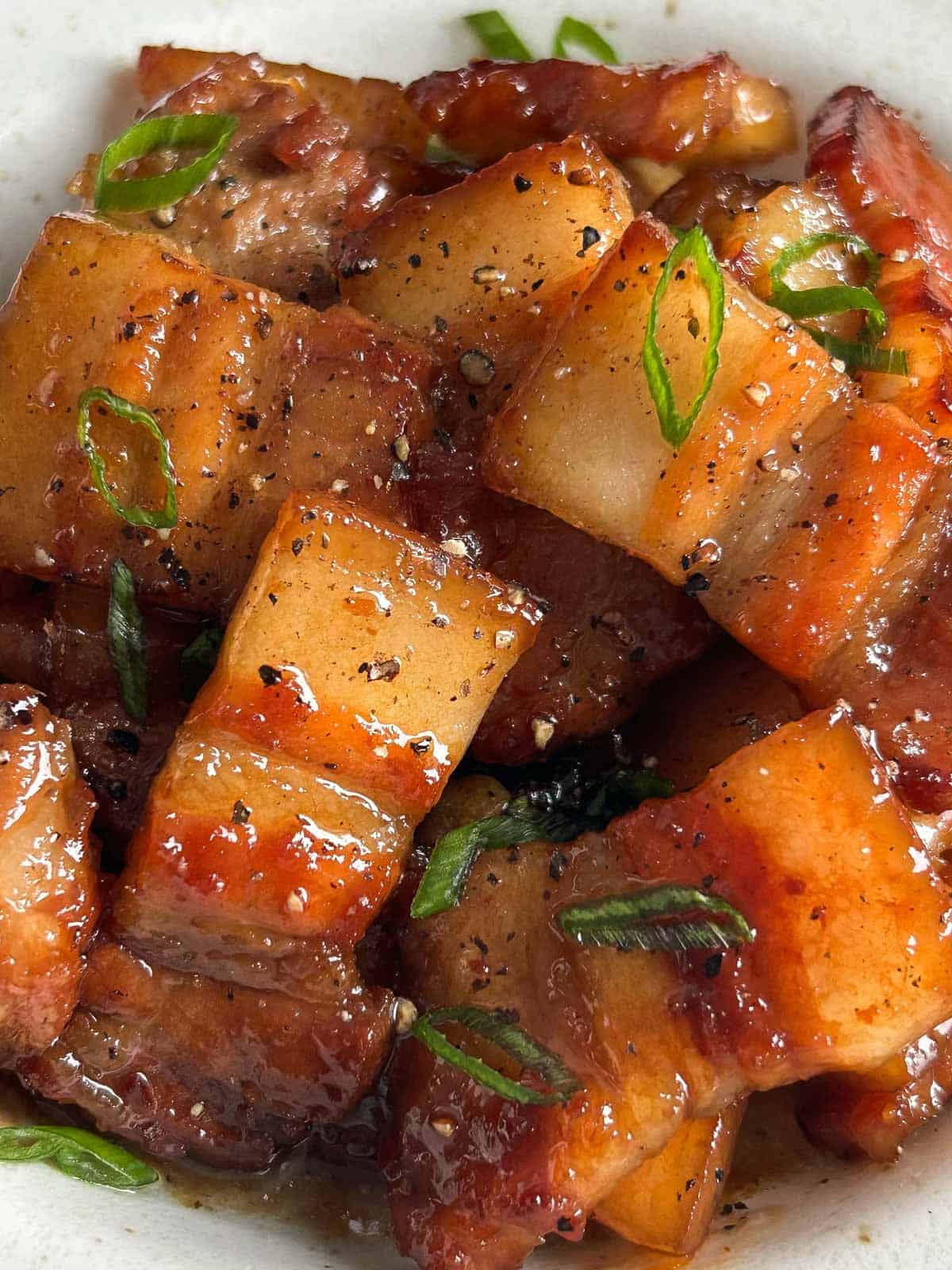 Caramelized pork belly in bowl garnished with scallions and black pepper.