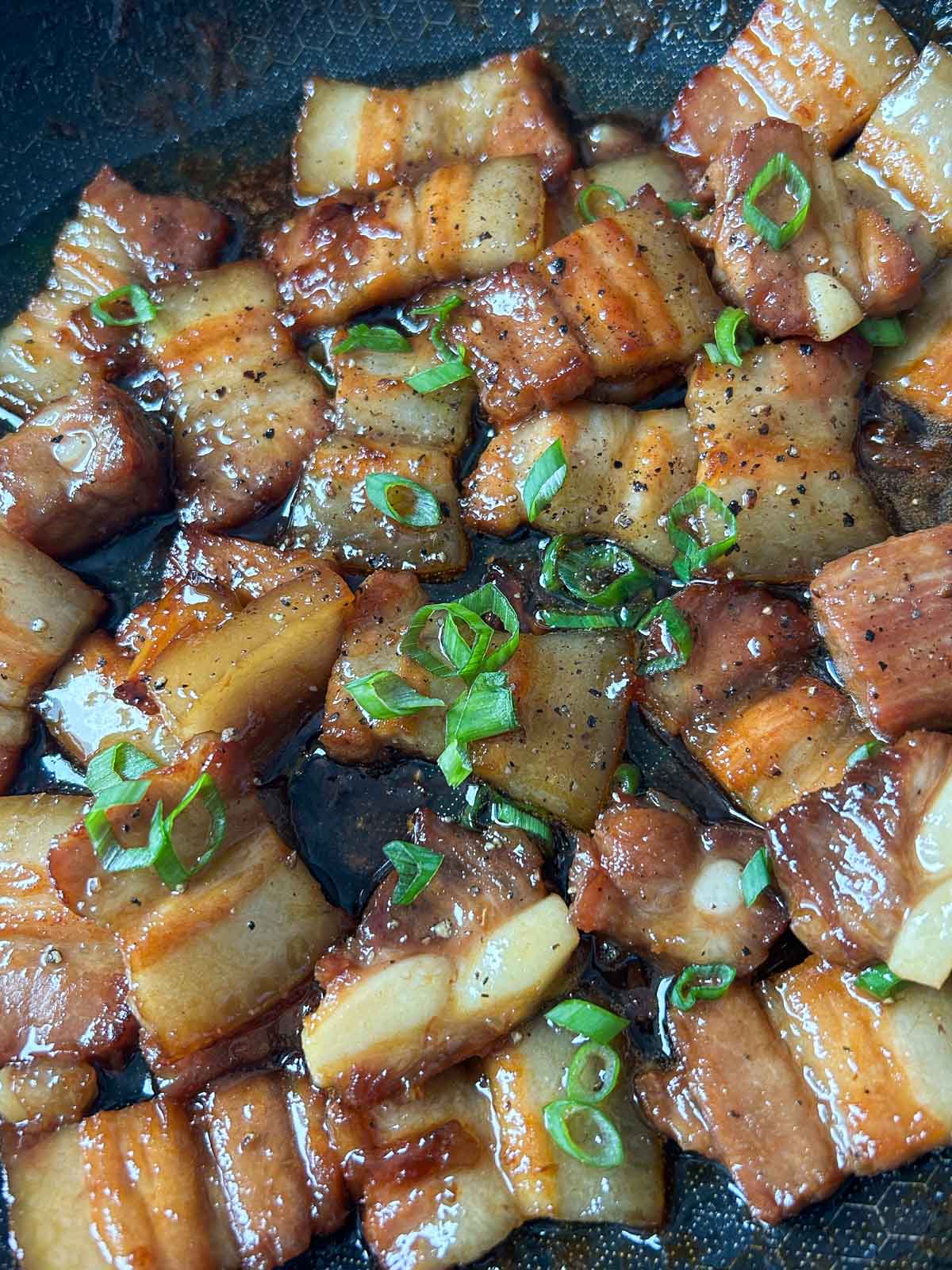 Caramelized pork belly in a pan with scallions and black pepper.