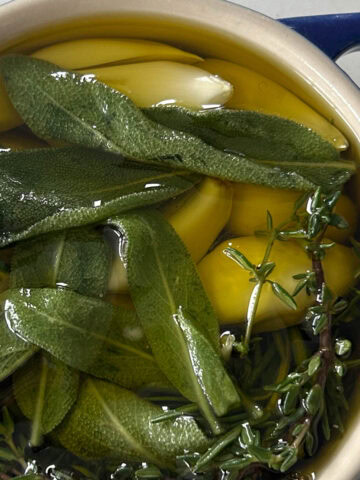 Zoomed in on the cocotte with oil, sage, thyme, garlic and rosemary in it.