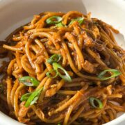 1x1 overhead shot of salmon garlic noodles plated in a bowl plate and garnished with scallions.