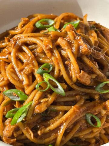 1x1 overhead shot of salmon garlic noodles plated in a bowl plate and garnished with scallions.