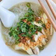 Overhead shot of Vietnamese chicken noodle soup with shredded chicken, bean thread noodles, cilantro, fried garlic, fried shallots, and scallions in a clear golden broth.