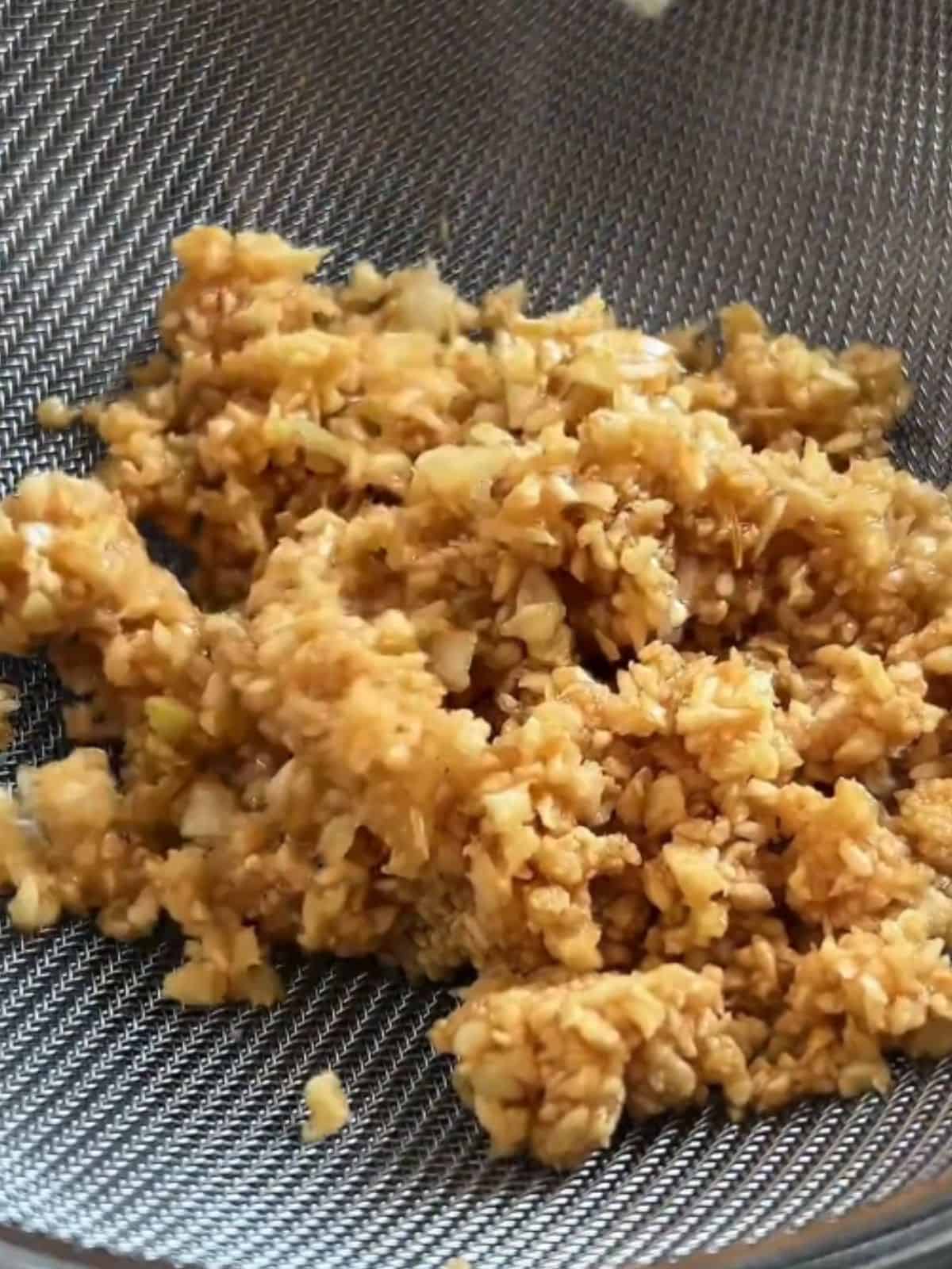 Close-up of crispy fried garlic draining in a fine mesh sieve, separating from the garlic oil.
