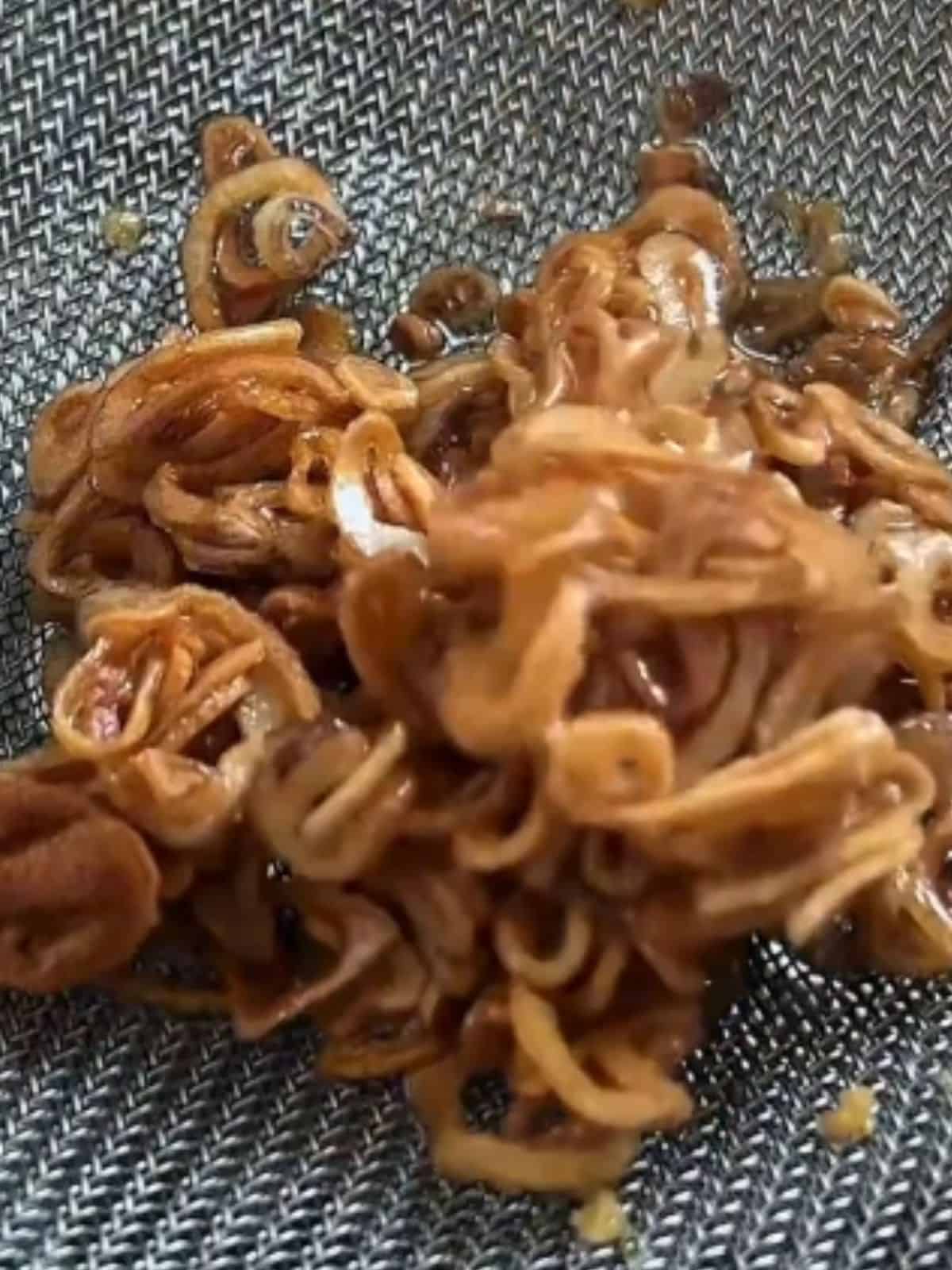 Close-up of golden fried shallots draining in a fine mesh sieve after being crisped in hot oil.