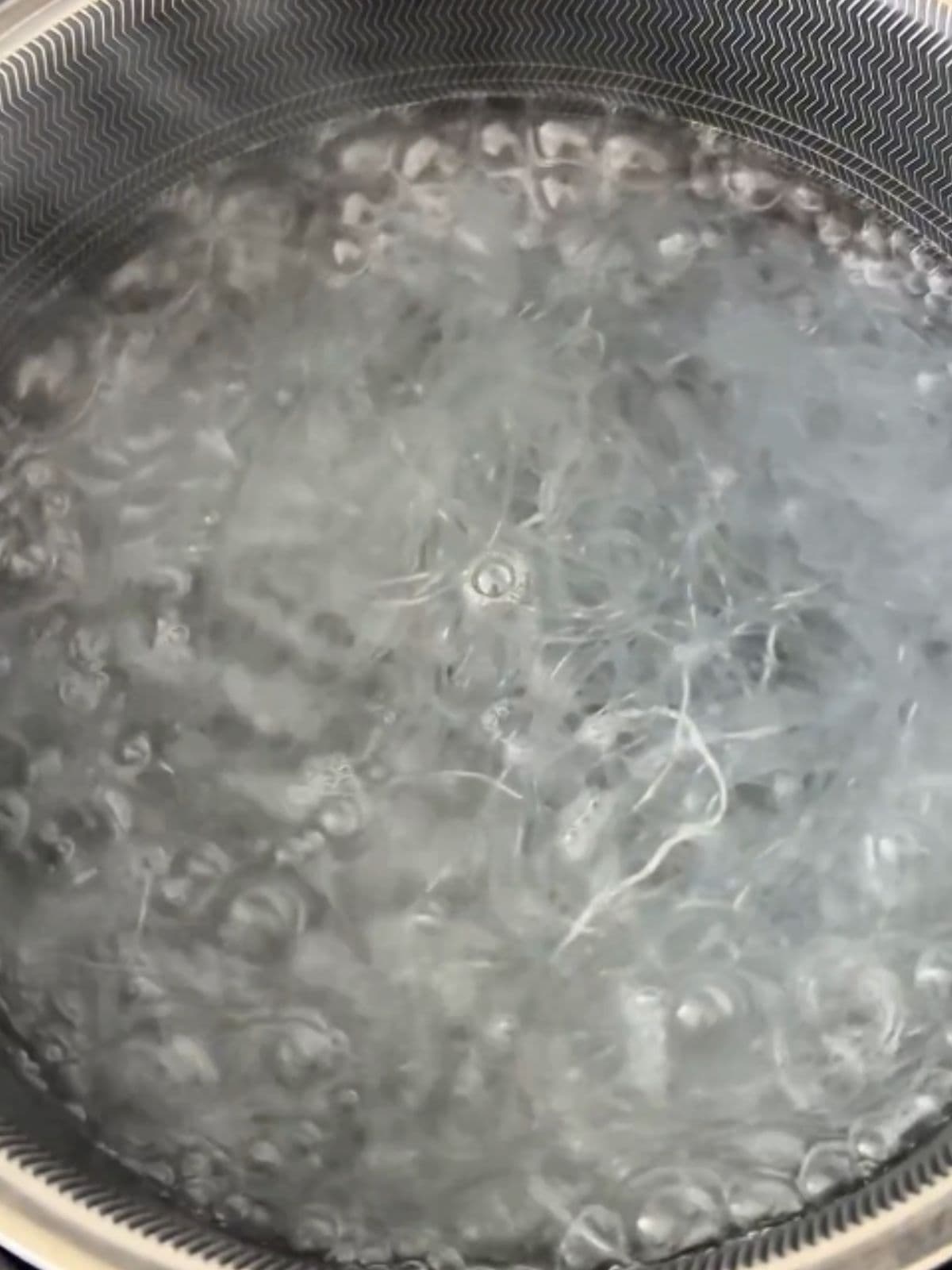 Overhead view of bean thread noodles boiling in a pot of water until softened and translucent.