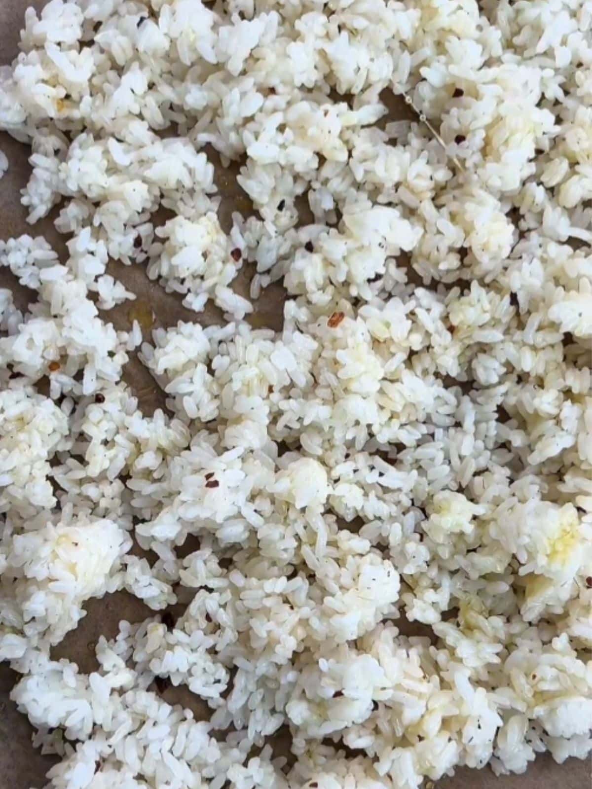Cooked white rice spread on a baking sheet with seasoning before baking.
