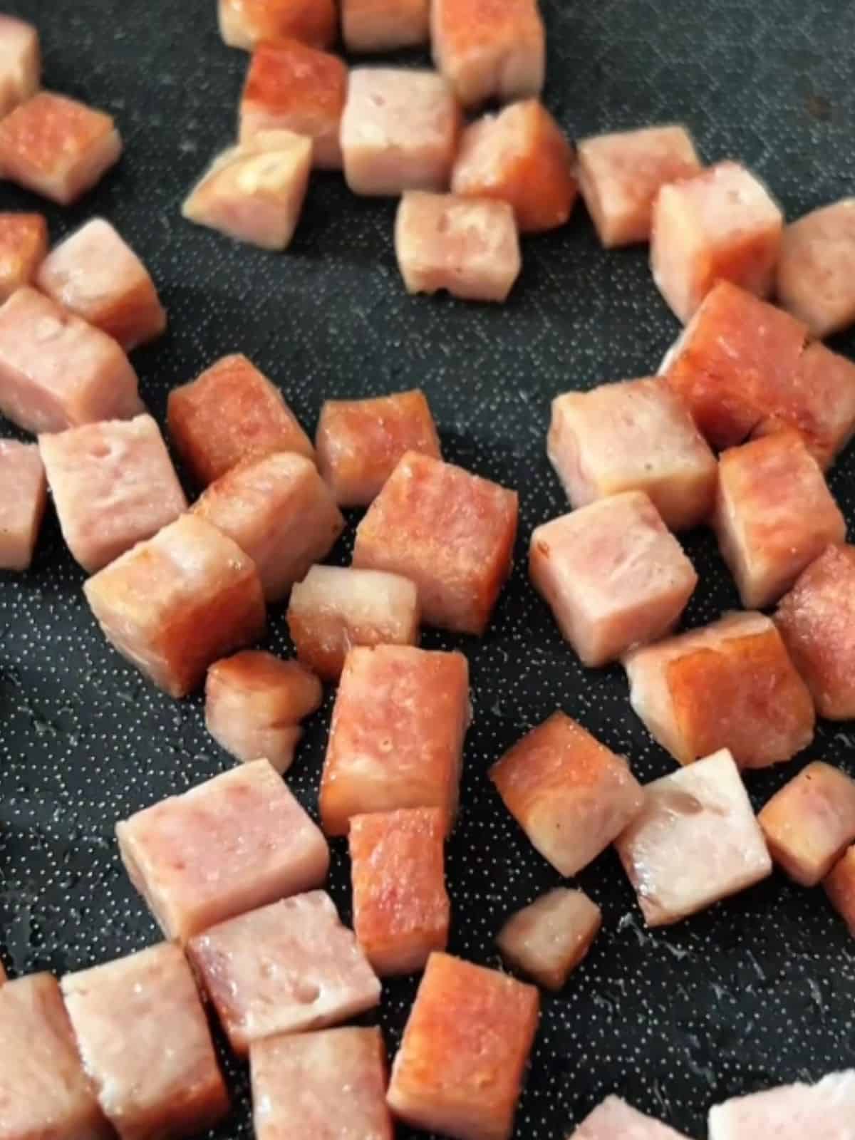 Cubed Spam being pan-fried until golden brown on all sides.