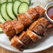 Crispy pork belly on a plate with cucumber, lettuce, noodles and fish sauce.