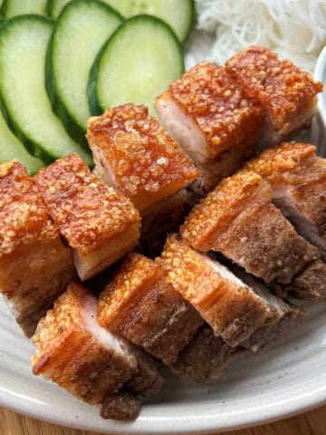 Crispy pork belly on a plate with cucumber, lettuce, noodles and fish sauce.
