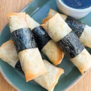 Spam musubi egg rolls on a plate with dipping sauce.