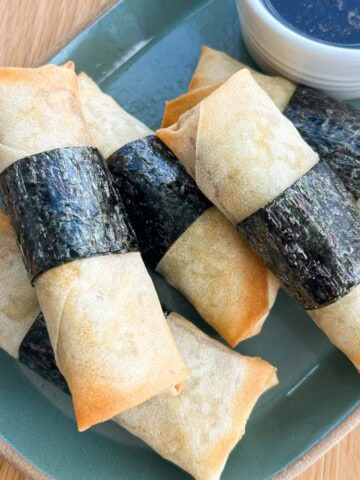 Spam musubi egg rolls on a plate with dipping sauce.