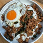 Pad kra pao over rice with a fried egg on top.