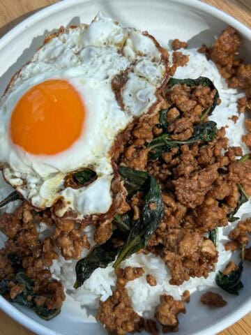 Pad kra pao over rice with a fried egg on top.
