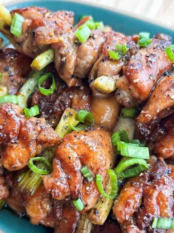 Vietnamese yakitori chicken skewers with a sticky fish sauce caramel glaze, topped with black pepper and sliced scallions on a plate.