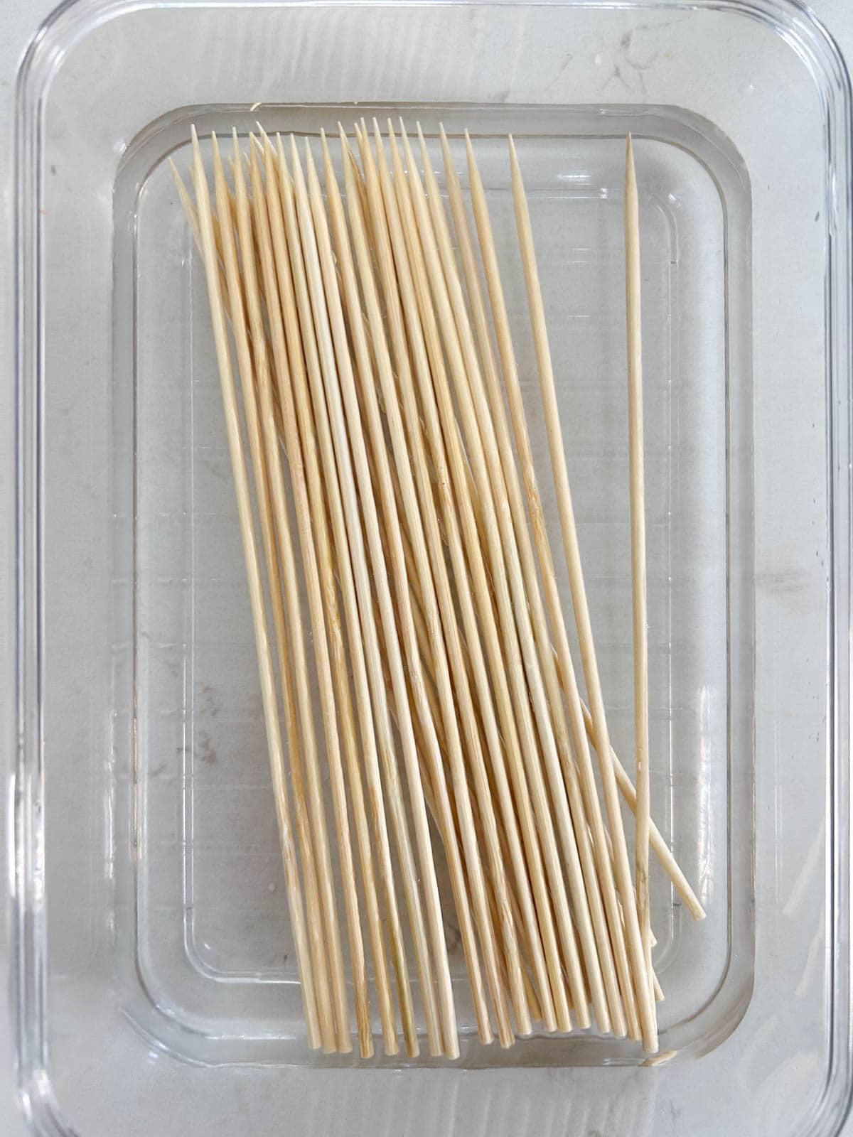 Bamboo skewers soaking in water in a clear glass container so they don't burn on the grill.