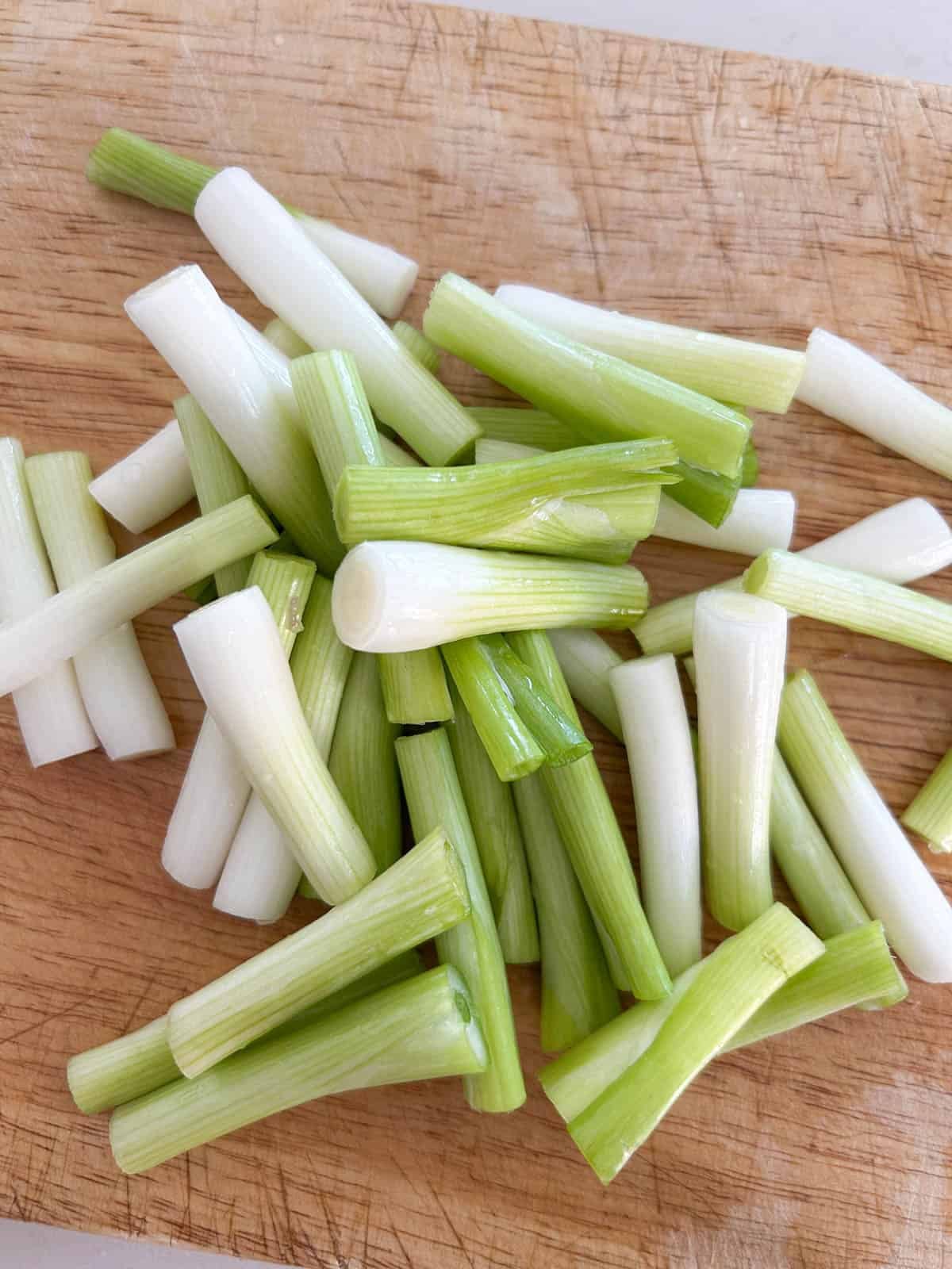 Scallions cut into 2-inch pieces on a wooden cutting board for chicken yakitori skewers.