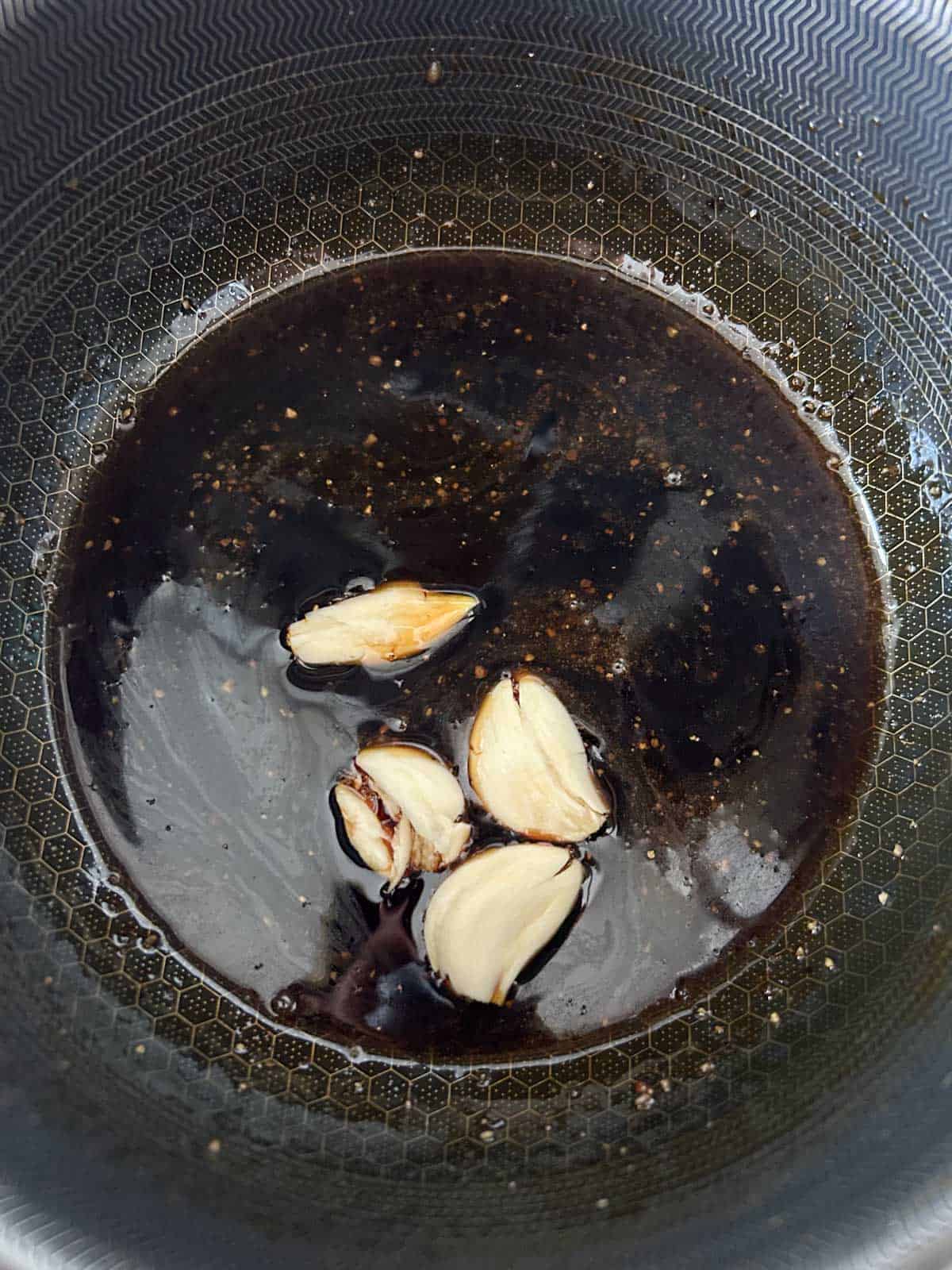 Fish sauce caramel glaze with smashed garlic cloves and black pepper in a pot.