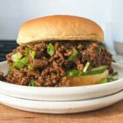 Vietnamese caramelized ground beef on a bun with cucumber slices and sliced scallions on a white plate.