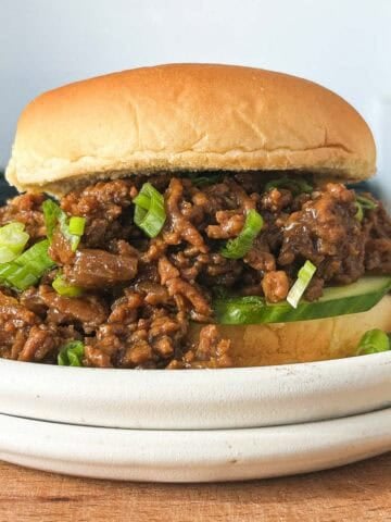 Vietnamese caramelized ground beef on a bun with cucumber slices and sliced scallions on a white plate.