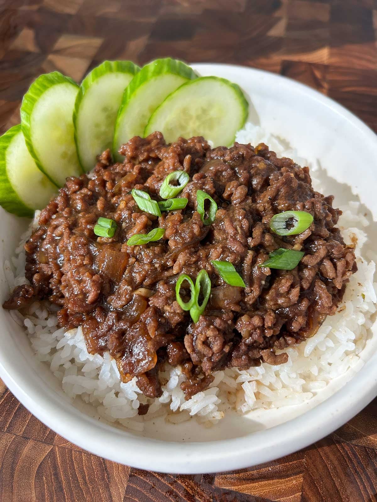 Bowl of jasmine rice topped with Vietnamese caramelized ground beef, scallions, and cucumber slices.