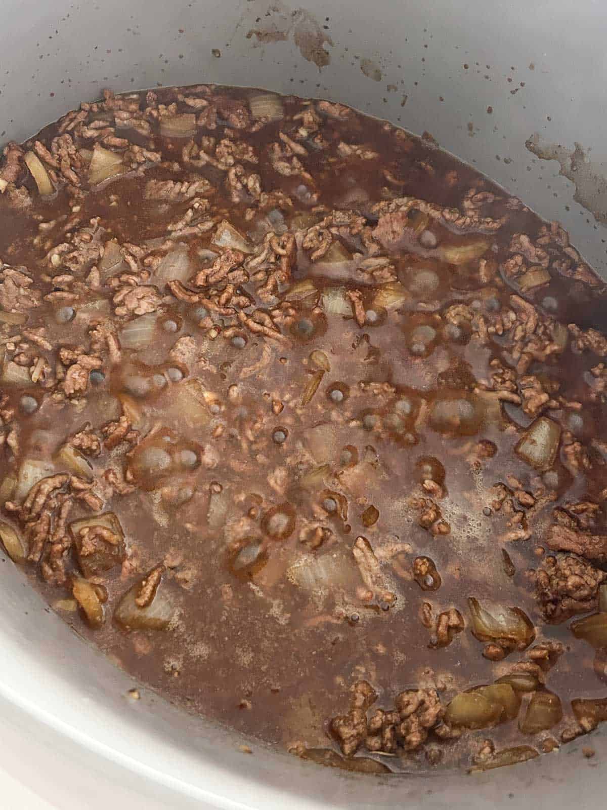 Browned ground beef and onions simmering in a dark caramel sauce with coconut water.