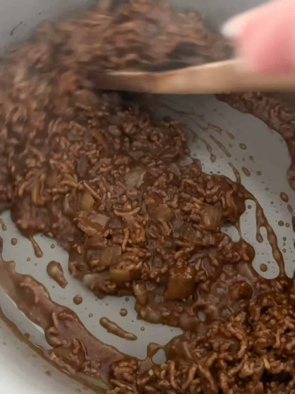 Wooden spoon stirring Vietnamese caramelized ground beef as the sauce thickens and coats the meat.