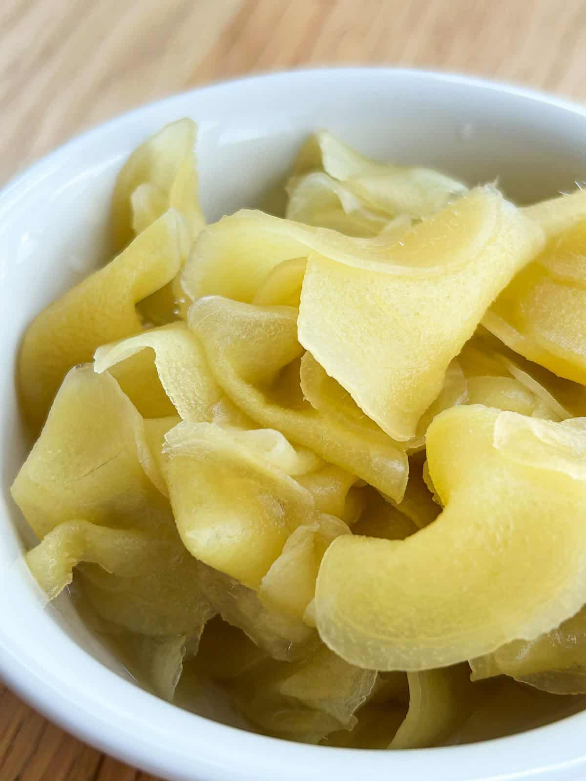 White bowl filled with pale yellow pickled ginger slices.