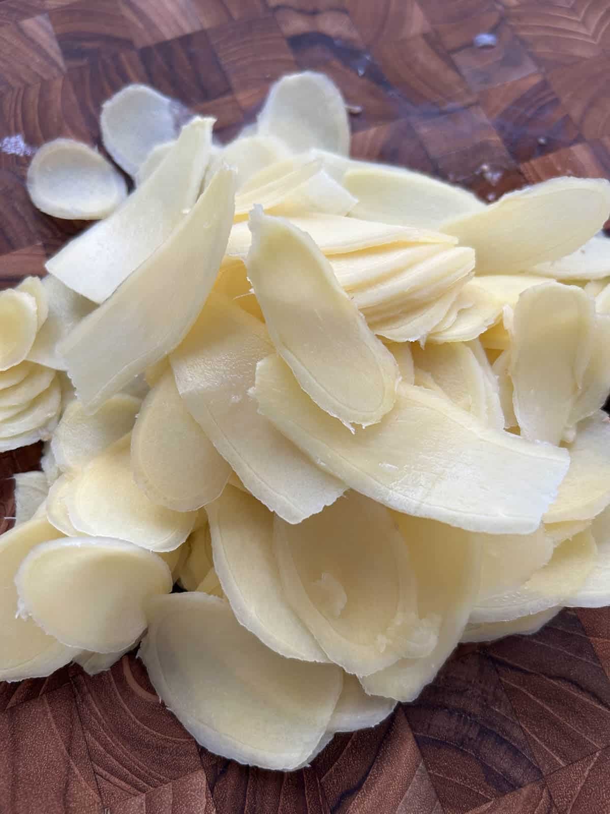 Pile of thinly sliced raw ginger on a wooden cutting board.